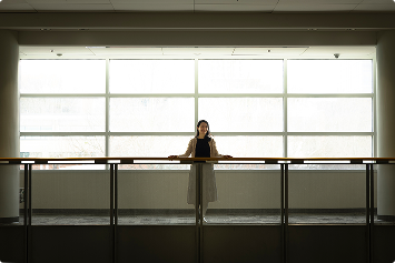 a student stands on a balcony with a wall of windows behind her
