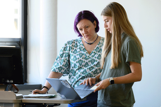 a student and her advisor discuss something on her laptop