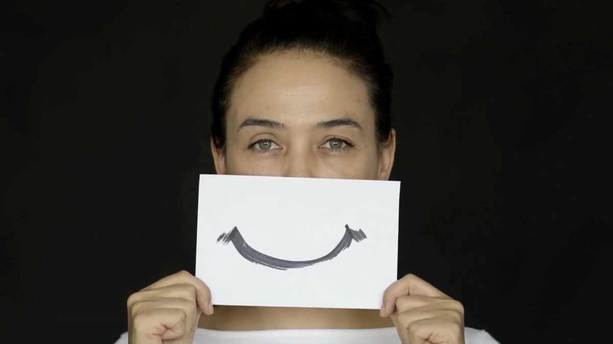 Person holding index card with hand drawn smile to cover actual mouth.